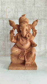 Hand-carved wooden statue of Lord Ganesha, seated with intricate details and traditional attire, against a light background.